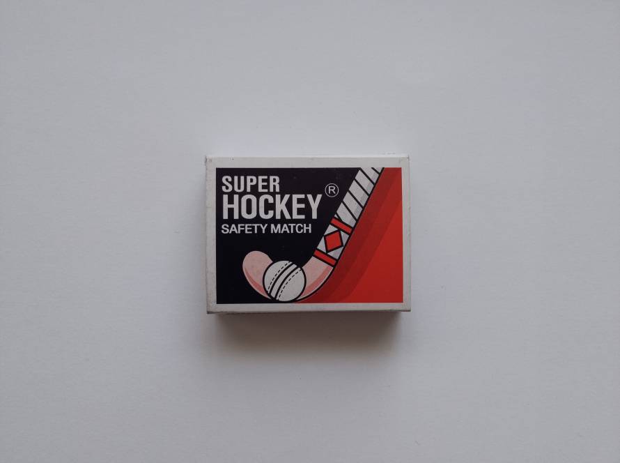 Sporty matchbox with a red and black graphic of a hockey stick and ball. Branded as 'Super Hockey'.