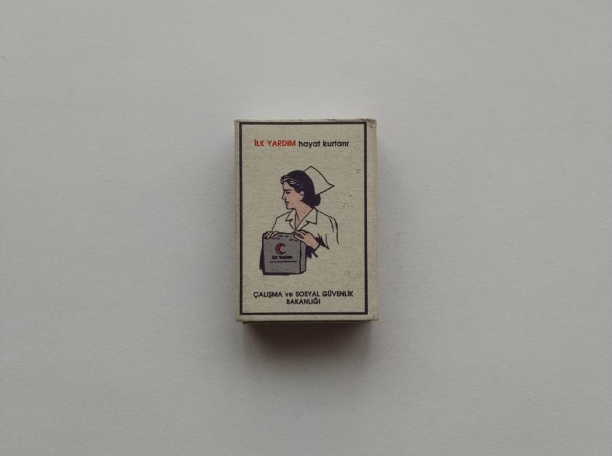 “İlk Yardım hayat kurtarır” awareness matchbox issued by Çalışma ve Sosyal Güvenlik Bakanlığı; nurse illustration holding first aid kit.