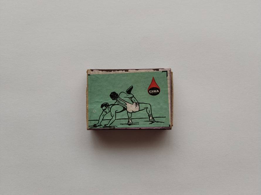 ÇIRA wrestling-themed matchbox illustrating traditional Greco-Roman style bout. Dynamic sports collectible.