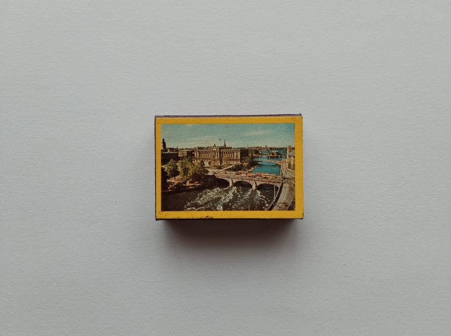 Scenic matchbox with a city bridge and waterfront view, likely Stockholm, framed with a yellow border.