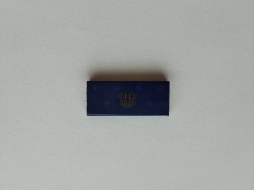 Dark blue matchbox with ornate “H” crest and subtle decorative pattern, likely hospitality branding.