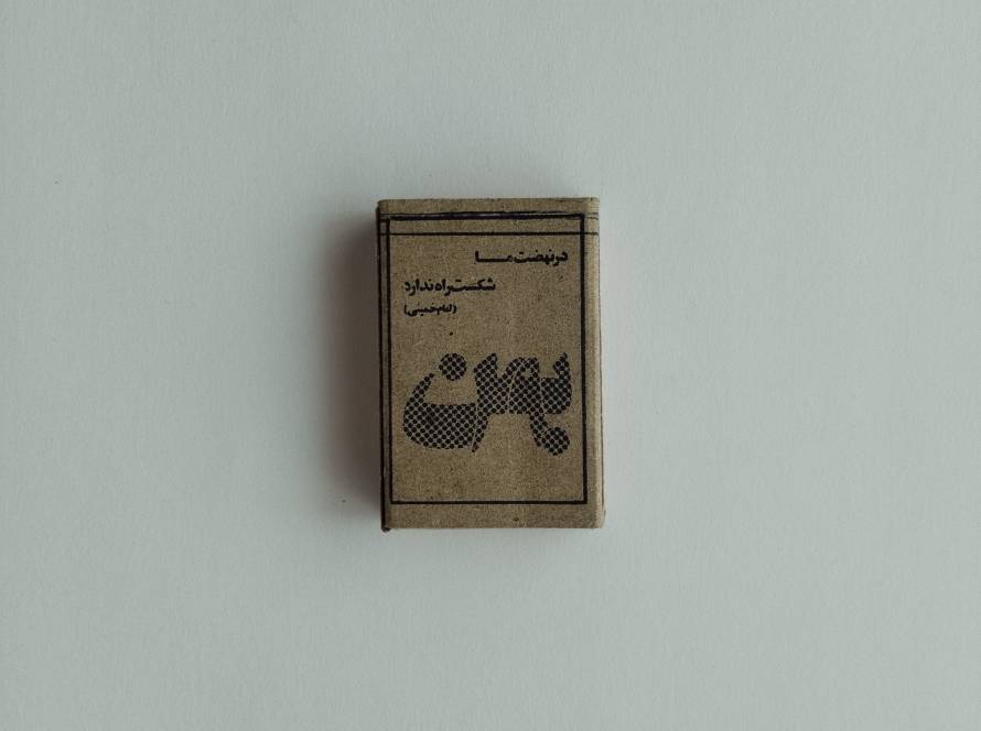 Vintage matchbox with Persian script and traditional monochrome design, showing signs of age and wear.