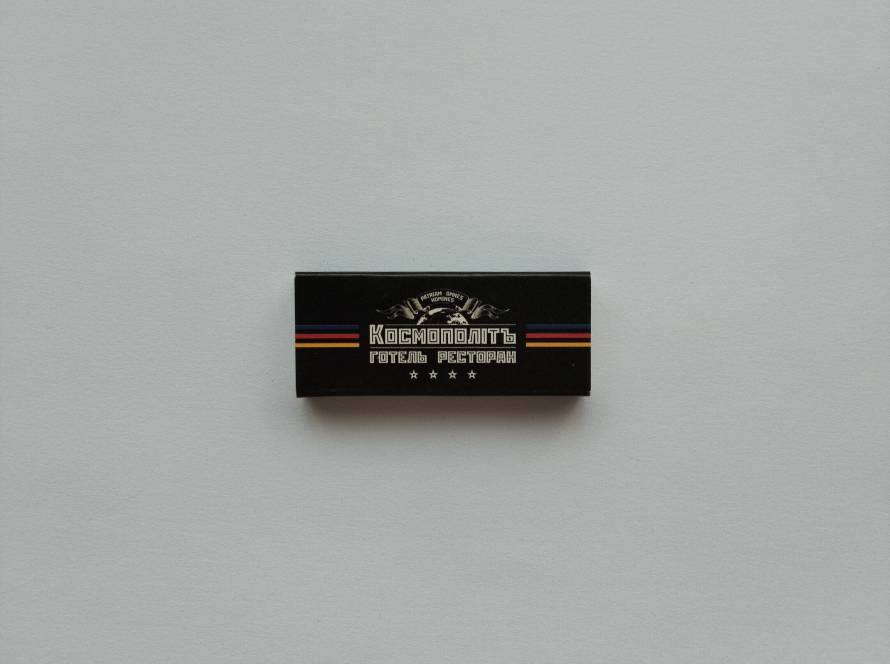 Promotional matchbox from Cosmopolite Hotel Restaurant in Kyiv, featuring Cyrillic branding and decorative stripes.