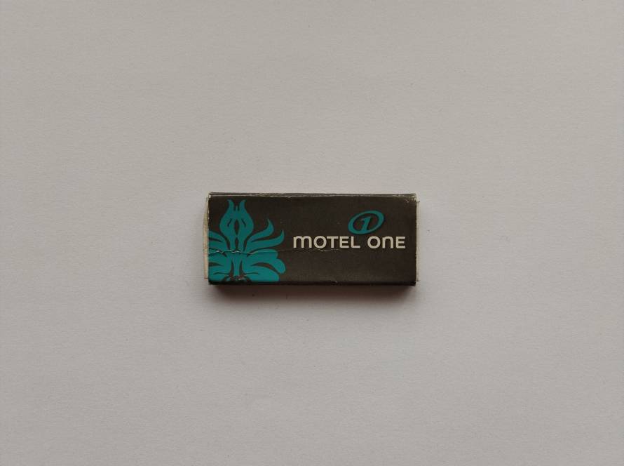 Motel One promotional matchbox featuring teal floral motif and modern dark-toned typography, consistent with contemporary budget-design hotel branding aesthetics.