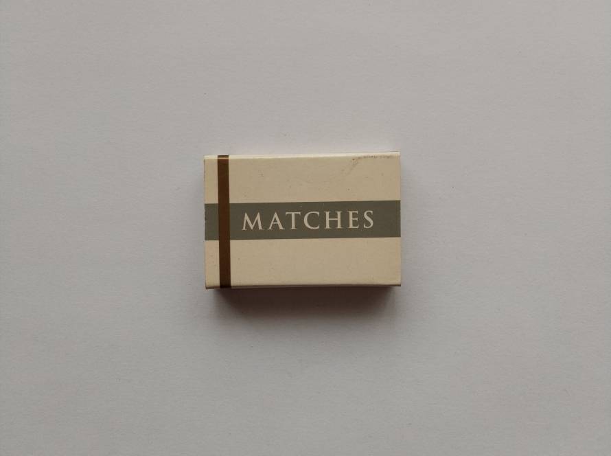 Minimalist beige matchbox with grey band and “MATCHES” text. Likely hotel or restaurant stock design. Simple, non-branded packaging.