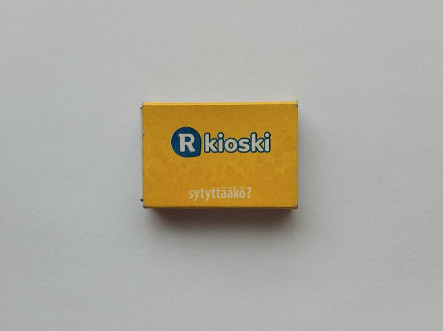 R-kioski promotional matchbox in bright yellow with Finnish slogan “sytyttääkö?”; retail advertising piece produced by Swedish Match, featuring modern branding.