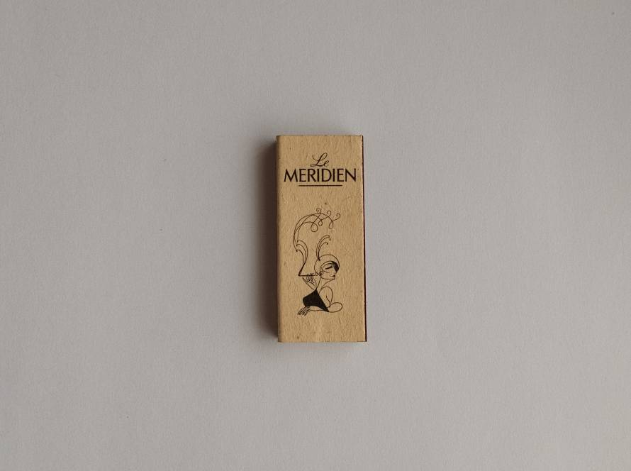 Elegant beige matchbox from “Le Méridien” featuring artistic illustration by Ken Maryanski. Refined hotel branding with collectible art element.