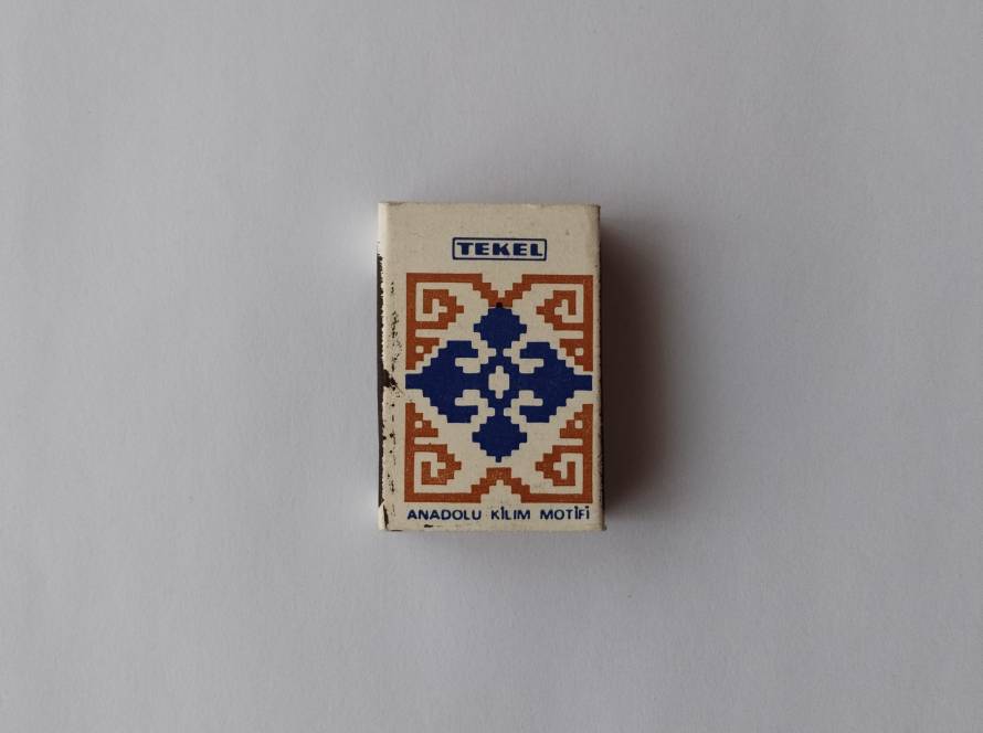 TEKEL branded matchbox displaying an Anatolian kilim motif in blue and orange. Represents traditional Turkish textile patterns and cultural heritage.