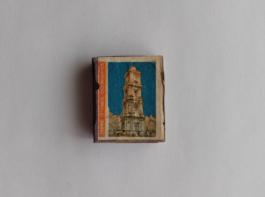 Vintage matchbox label depicting Dolmabahçe Clock Tower in Istanbul with a deep blue background and aged print texture.