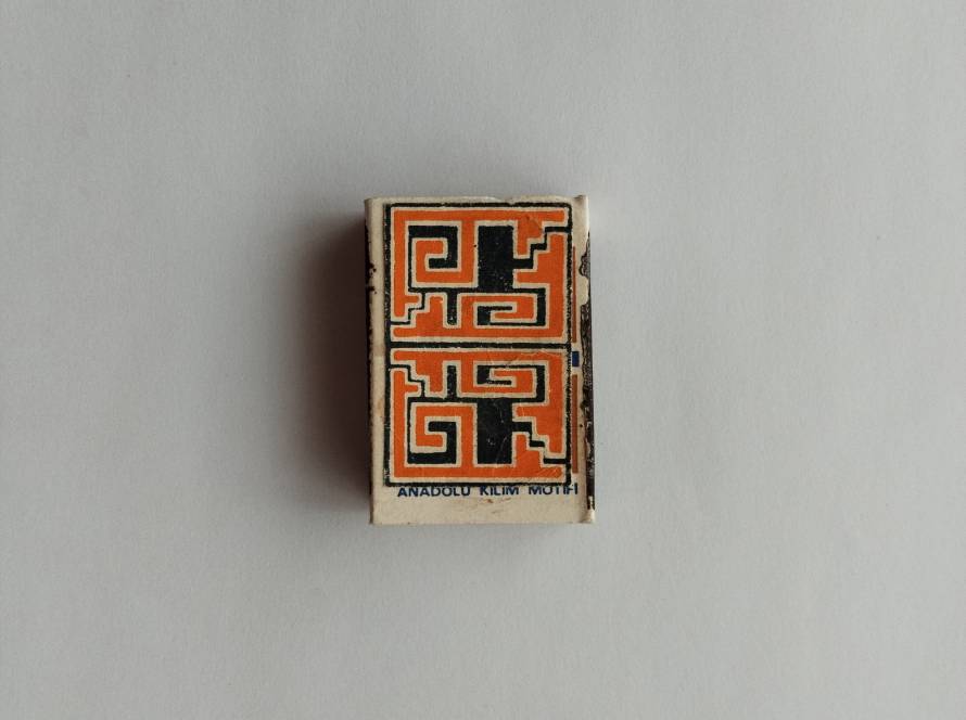 Tekel geometric motif matchbox with bold black and orange Anatolian-inspired design; reverse includes 1986 production marking and repeating Tekel branding.