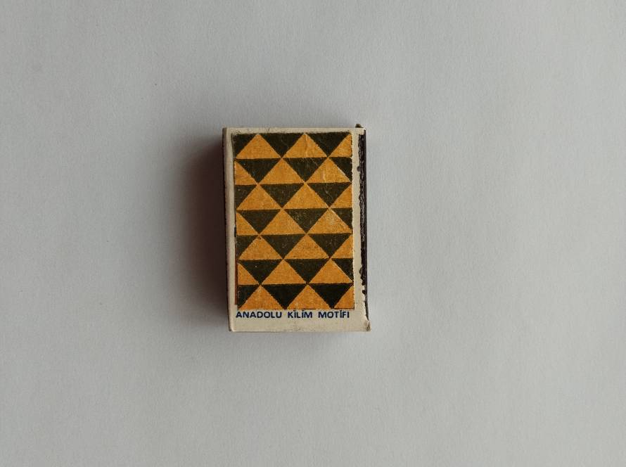 Tekel “Anadolu Kilim Motifi” matchbox featuring repeating yellow and dark geometric triangle pattern; reverse marked with 1986 production information.