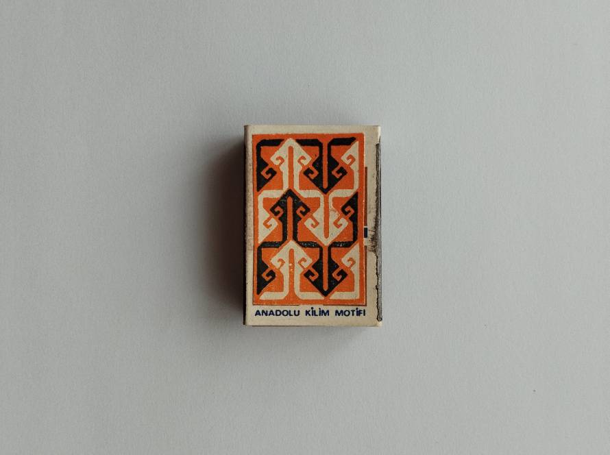 Decorative orange-and-black Anadolu kilim motif matchbox with tribal-inspired pattern.