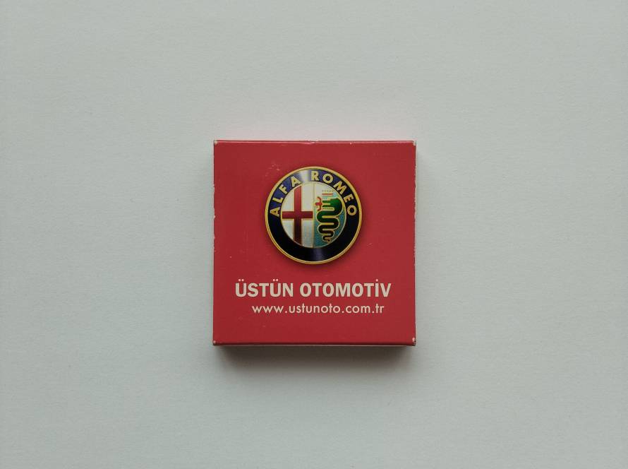 Üstün Otomotiv promotional matchbox featuring the Alfa Romeo logo, dealership branding and website information.