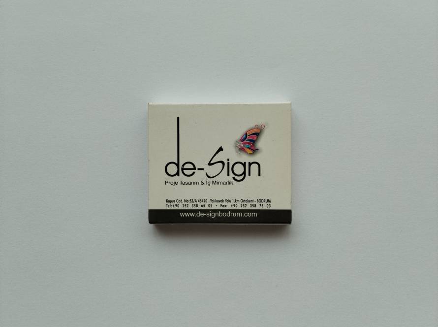 De-Sign Proje Tasarım & İç Mimarlık promotional matchbox from Bodrum featuring colorful butterfly logo, company website and contact details.