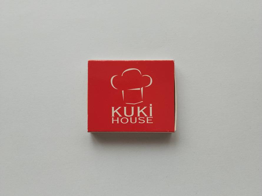 Promotional matchbox for Kuki House bakery and pastry brand, featuring chef hat logo on bright red background.