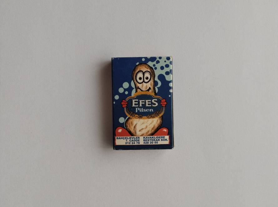 Humorous promotional matchbox advertising Efes Pilsen through the Vermişli pub chain, featuring a cartoon peanut mascot and location details for Ankara branches.