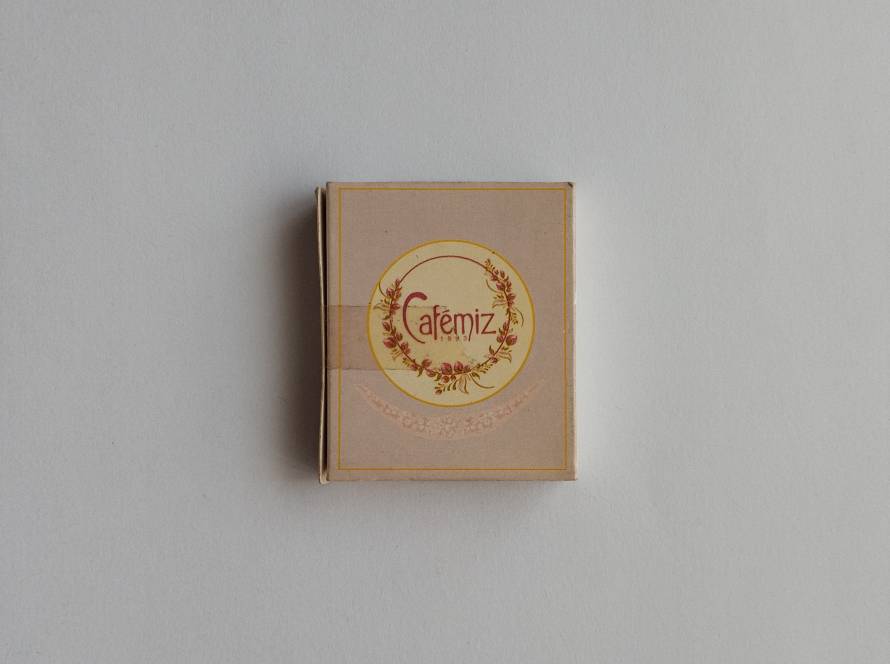 Promotional matchbox for Cafemiz, featuring an elegant floral wreath logo and soft pastel design associated with café and hospitality branding.