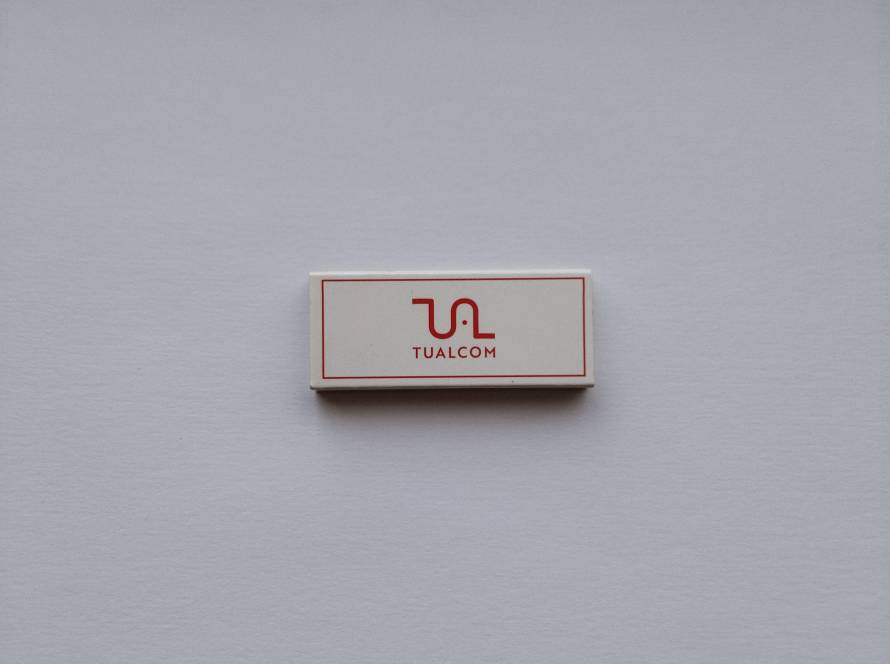 Promotional matchbox for TUALCOM, featuring the company's red-and-white logo on a clean minimalist design. Corporate advertising issue in excellent condition.