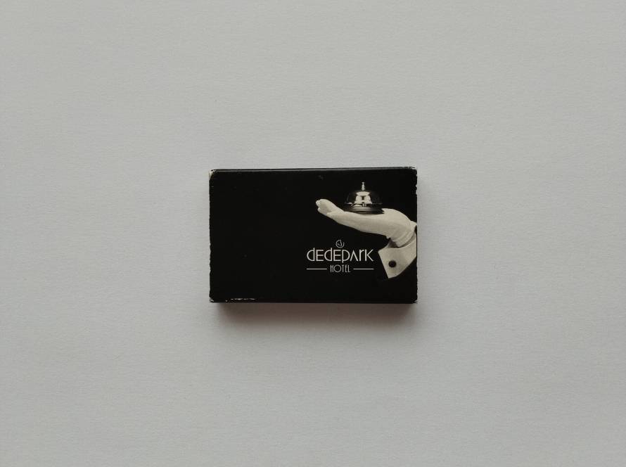 Promotional matchbox for Dedepark Hotel featuring an elegant bell-service graphic on the front in a minimalist black design.