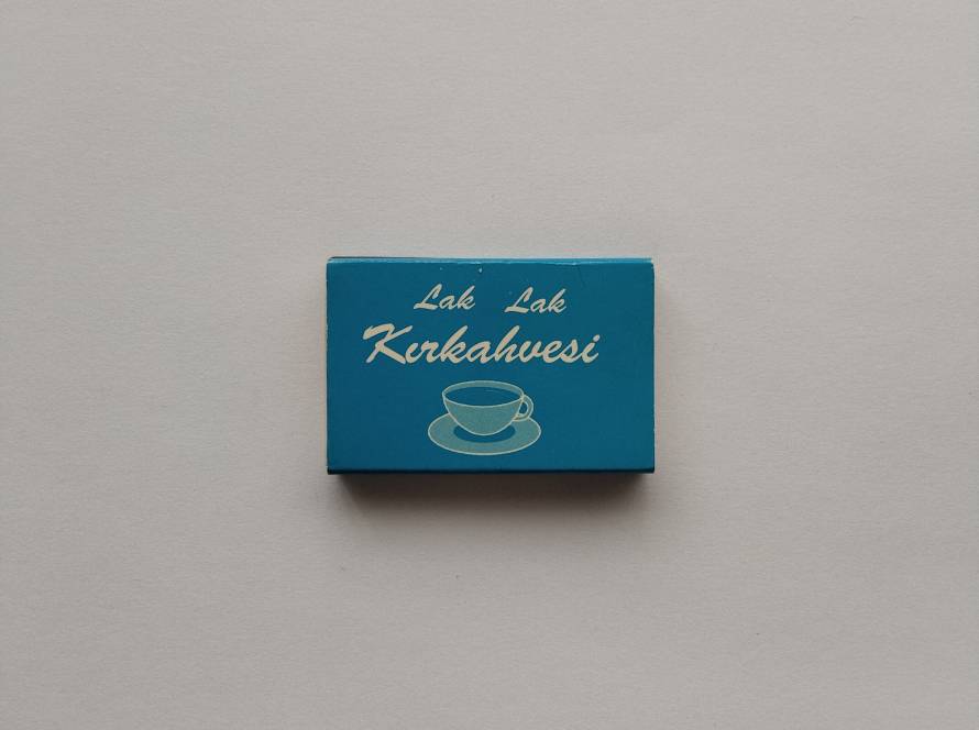 Promotional matchbox for Lak Lak Kırkahvesi. Features a bright turquoise design with a coffee cup illustration, promoting a traditional Turkish coffeehouse and fortune-telling café. Collectible café advertising piece.
